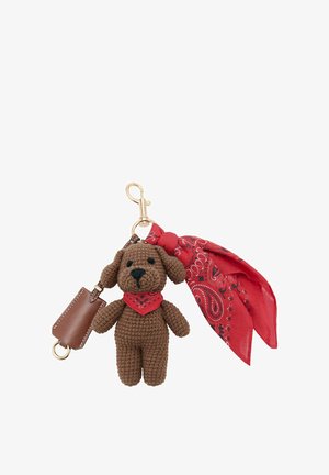Porte-clés chien en crochet marron avec bandana rouge autour du cou, attaché à un clip doré avec accessoire en tissu rouge à motifs et petite pochette marron.