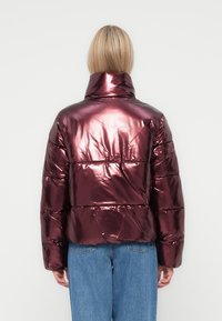 Metalická burgundská puffer bunda s vysokým límcem, prošívaným designem a elastickým lemem. Nosit s modrými džínami, které mají texturovaný povrch.