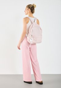Sac à dos en vichy rose avec poche avant, fermeture par cordon de serrage et porte-clés en peluche. Pantalon large à rayures roses et débardeur blanc ajusté.