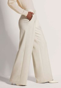 Wijdne pants in lichtbeige stof met een subtiele textuur. Bevat voorzakken en een knoopsluiting bij de taille.