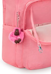 Růžový batoh vyrobený z odolného materiálu, s přední kapsou na zip, dekorativním chlupatým klíčenkovým opicí a vnější boční kapsou.
