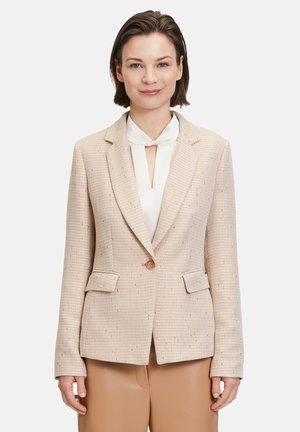 Hellbeige Blazer mit Fischgrätenmuster, Reverskragen, einem Knopfverschluss und zwei Fronttaschen, über einer weißen Bluse getragen.