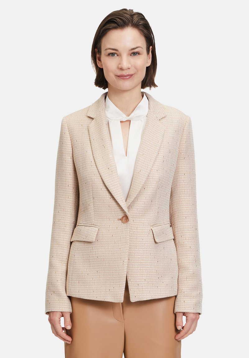 Hellbeige Blazer mit Fischgrätenmuster, Reverskragen, einem Knopfverschluss und zwei Fronttaschen, über einer weißen Bluse getragen.