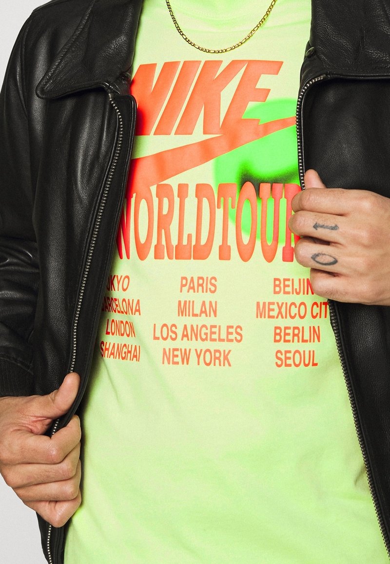 Černá kožená bunda přes neonově zelené tričko s oranžovým textem "NIKE WORLDTOUR" a názvy měst tučně vytištěnými vertikálně.