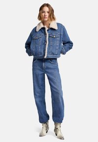 Przycięta dżinsowa kurtka z wełnianym kołnierzem, w połączeniu z dżinsowymi spodniami z wysokim stanem. Posiada klasyczne kieszenie i luźny krój. Botki w wężowy wzór.