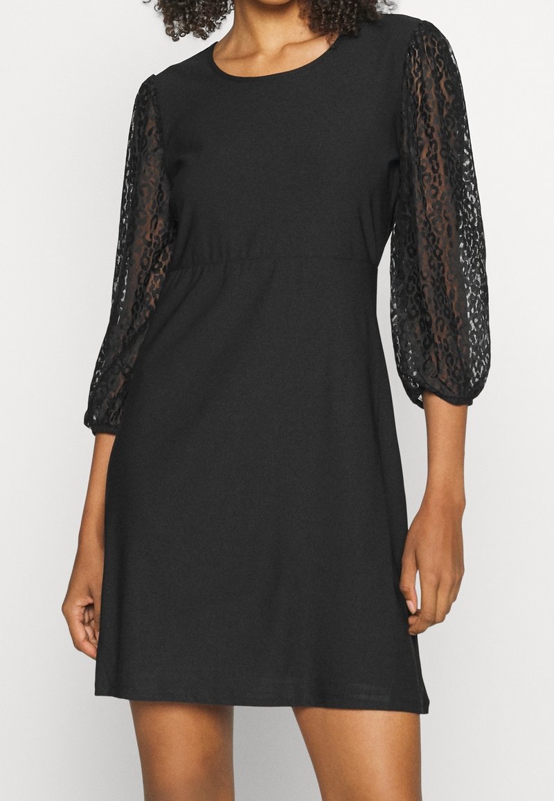 Vestido negro con escote redondo, cuerpo corto y mangas abullonadas de encaje transparente con un patrón texturizado. Tela suave con cintura elástica.