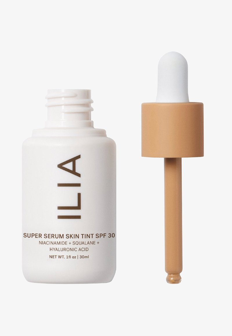 ILIA Super Serum Skin Tint SPF 30 in una bottiglia di vetro bianca, con un tappo a contagocce. Testo sulla bottiglia in marrone. Contiene niacinamide e squalano.