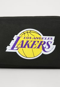 Los Angeles Lakers logo med lilla tekst over en gul basketball på en sort tekstureret stofbaggrund.