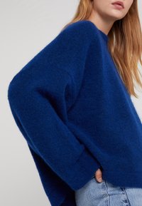 Blauer Wollpullover mit lässiger Passform, überschnittenen Schultern und gerippten Bündchen. Die Textur ist weich und flauschig, mit einem geraden Saum.