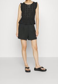 Černý peplum top s volánkovými rukávy a strukturovanou látkou, doplněný o černé strukturované šortky a ploché černé sandály.