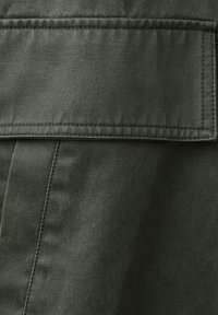 Približek temno zelene tkanine z veliko pravokotno preklopno žepno loputo, ki ima vidne šive in detajle šivov.