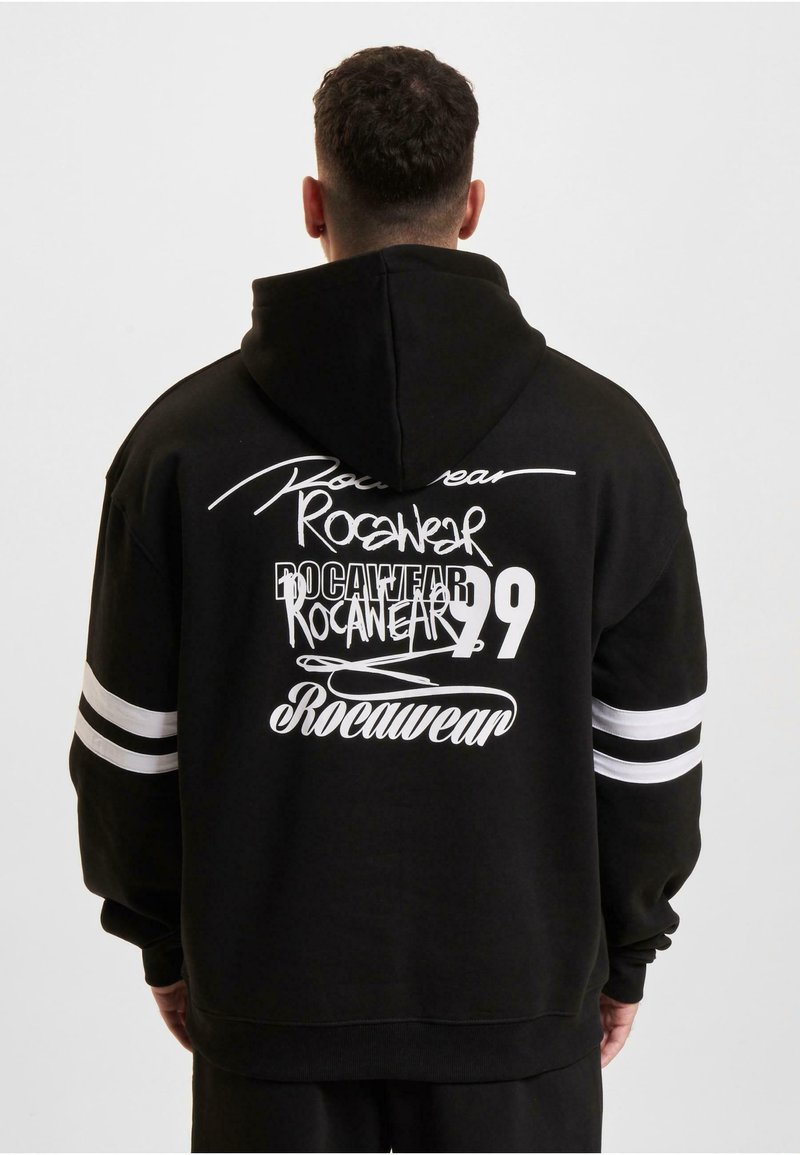 Crna kapuljača s bijelim grafičkim tekstom, uključujući "Rocawear" i broj "99." Dizajnirana sa dvije bijele pruge na svakoj rukavu.