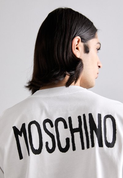 White cotton t-shirt featuring large black "MOSCHINO" text on the back. Crew neck design with short sleeves and a relaxed fit.