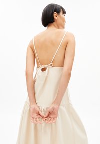Beiges Baumwollkleid mit tiefem Rückenausschnitt, verstellbaren Spaghettiträgern und gerafftem Saum. Mit einer gebundenen Detail hinten. Glatte Textur.