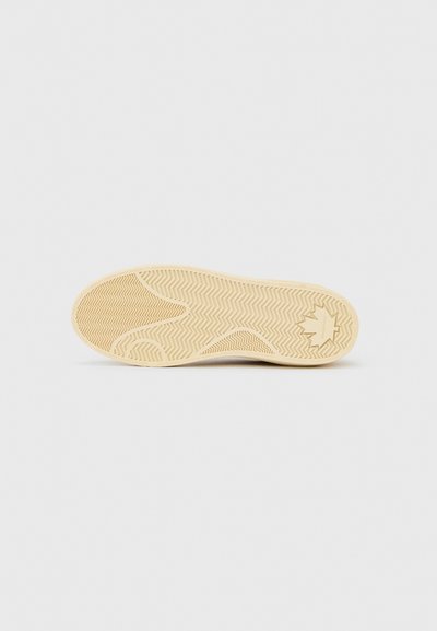 Talpă de pantof sport din cauciuc în bej pal. Prezintă un model de tracțiune de tip herringbone, margini netede și un accent logo central. Design texturat pentru aderență.