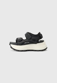 Sandalha preta com duas tiras ajustáveis em Velcro, parte superior em malha acolchoada e sola branca robusta. Apresenta um padrão texturizado para maior aderência.