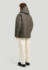 Olivgrön puffjacka med stor huva, vadderad design och slät yta. Bärs över vita vida byxor och svarta plattformsstövlar.