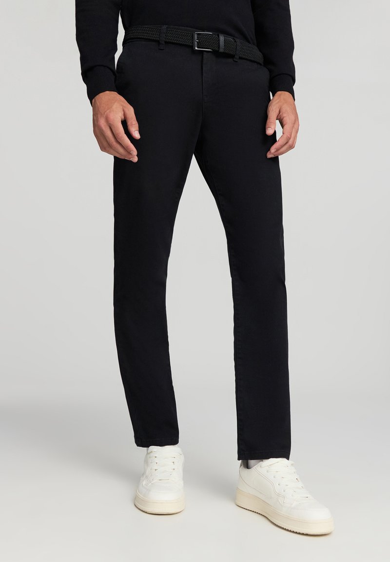 Czarne bawełniane spodnie o slim fit, z tkaną paskiem o fakturze. W połączeniu z białymi trampkami, wygląd jest swobodny i nowoczesny.