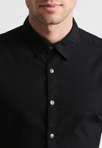 Zwarte overhemd met knopen en een kraag, voorzien van een gladde textuur, zichtbare knoopdetails en een getailleerde pasvorm.