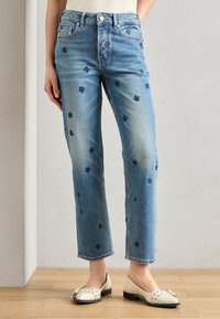 Lyse blå denimjeans med rett benkutt, med små mørkeblå blomsterbroderier og slitte detaljer nær kanten og lommene.