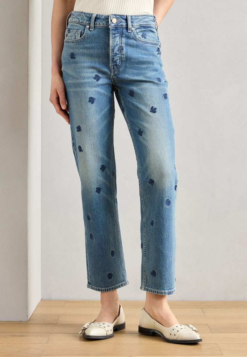 Lyse blå denimjeans med rett benkutt, med små mørkeblå blomsterbroderier og slitte detaljer nær kanten og lommene.
