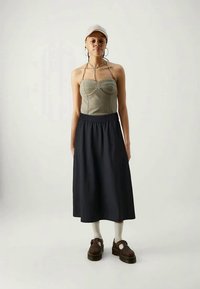 Top verde ajustado com costuras discretas, emparelhado com uma saia preta a extensão total. Sapatos plataforma castanhos e meias brancas completam o visual.