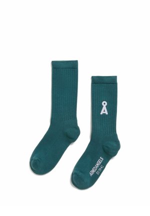 Zwei türkisfarbene gerippte Crew-Socken, eine mit weißem Logo nahe der Oberseite und Markenname mit Größe auf der Sohle gedruckt, auf weißem Hintergrund.