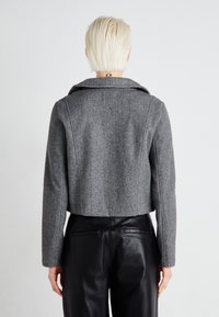 Grey cropped wool blend jacket with a wide collar, featuring structured seams and a back vent, paired with black leather pants.