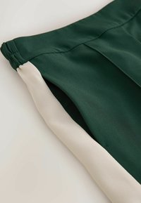 Shorts verts avec une bande latérale blanche et une ceinture élastique, présentés en gros plan sur un fond clair.