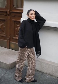 Suéter negro de gran tamaño con cuello alto, acompañado de pantalones sueltos de estampado de leopardo. Botines negros y una bufanda negra con flecos.