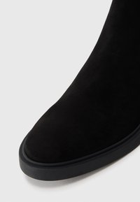 Cizme negre din suede, cu vârful rotund, având un superior texturat și o talpă robustă din cauciuc negru. Vedere de aproape care evidențiază detaliile.