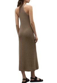 Mujer vistiendo un vestido midi marrón sin mangas y de canalé con un cuello alto, combinado con sandalias planas negras, vista desde atrás.