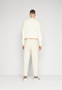 Biała, długosleeve bluza i dopasowane spodnie zwężane. Miękka tkanina o gładkiej fakturze, noszona z szaro-białymi trampkami.