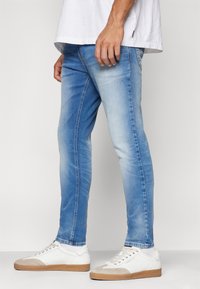 Ljust blå jeans i denim, med slim fit, ljusnande mönster och sömnadsdetaljer, kombinerade med vita och beige sneakers.