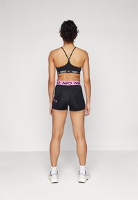 Reggiseno sportivo nero con spalline incrociate e logo Nike bianco, abbinato a pantaloni corti neri con vita rosa e dettaglio del logo.
