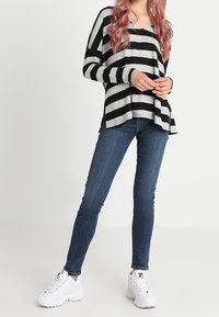 Schwarz-grau gestreiftes Langarmshirt, kombiniert mit einem engen blauen Jeans und weißen Sneakern, mit einem lässigen Saum und seitlichen Nähten.