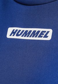 Blå textil med ett andningsbart nätmönster, med en framträdande vit "HUMMEL"-logotyp centralt placerad.