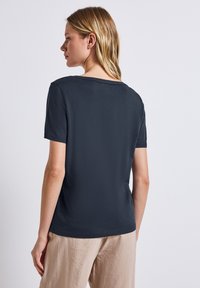 Tmavě šedé tričko s krátkým rukávem a kulatým výstřihem, s hladkou strukturou a volným střihem, nošené s světle zbarvenými texturovanými kalhotami.