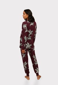 Two-piece maroon pajama set featuring a leaf pattern. Made of soft fabric, it has a relaxed fit with ribbed cuffs and a collared top.