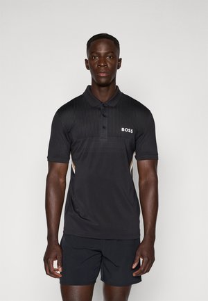 Svart pikétröja med texturerad design, tre knappar, logo på bröstet och kontrasterande sidostripes. Bärs med svarta shorts.