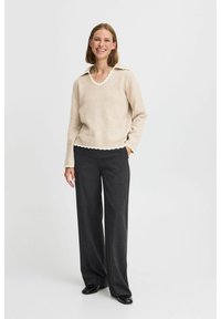Beige stickad tröja med en vågig krage, i kombination med skräddarsydda mörkgrå vida byxor. Slät textur, avslappnad passform.