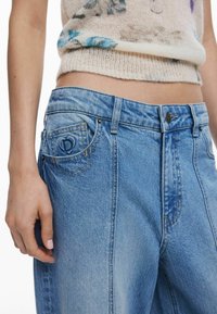 Hellblaue Denim-Jeans mit hoher Taille, versehen mit einem kleinen Logo auf der Gesäßtasche und kontrastierenden goldenen Nähten entlang der Nähte.