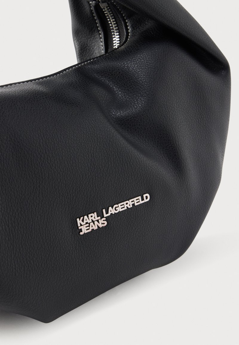 Bolso de mano de cuero negro texturizado con cremallera plateada y logotipo metálico "KARL LAGERFELD JEANS" en la parte frontal.