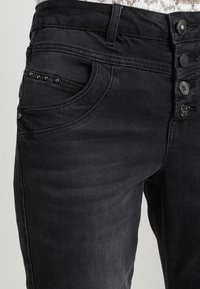 Černé džíny z denimu s přiléhavým střihem, pěti kapsami, diskrétními nýtkovými detaily na přední kapse a několika knoflíkovými uzávěry.