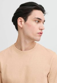 Beige cotton T-shirt with a classic crew neck, smooth texture, and relaxed fit, shown on a model from a side profile with dark hair.