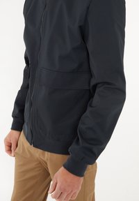 Giacca blu navy con chiusura a zip, polsini a costine e tasca frontale, realizzata in tessuto leggero e liscio. Adatta per un look casual.