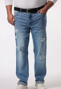 Jeans de mezclilla azul claro desgastados con un corte recto, que presentan desgarros en los muslos, un cinturón negro y puños enrollados sobre zapatillas blancas.