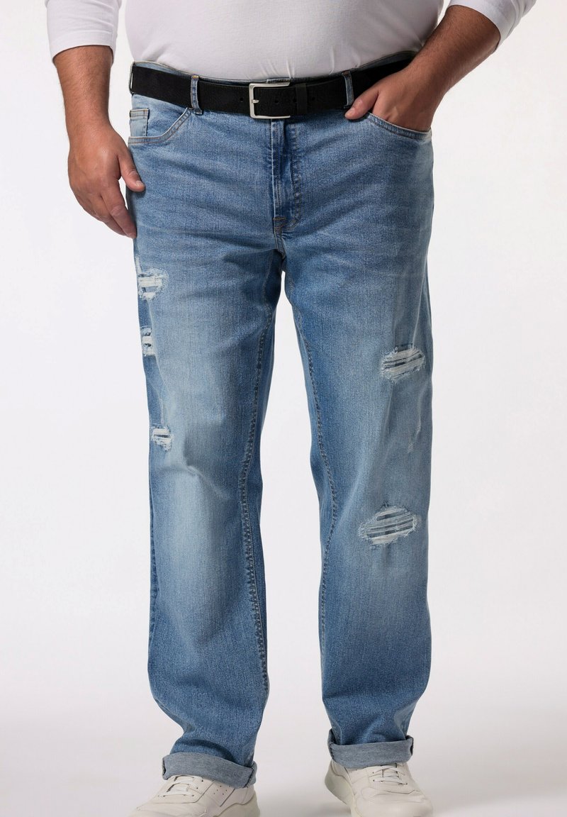 Jeans de mezclilla azul claro desgastados con un corte recto, que presentan desgarros en los muslos, un cinturón negro y puños enrollados sobre zapatillas blancas.