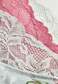 Tissu en dentelle présentant des motifs floraux roses et blancs, avec des détails et des textures complexes, superposé à un tissu doux en bas.