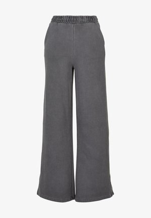 Laiene jalad hallides dressipükstes, mis on valmistatud pehmest kangast ja millel on mugav elastne vöökoht. Sile tekstuur, ilma nähtavate mustrite või aktsentideta.